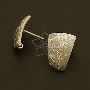 May include: A pair of silver earrings with a textured, abstract design. The earrings are shaped like a curved rectangle and a slightly curved rectangle.