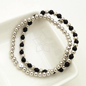 May include: A double-strand bracelet with black and silver beads. The bracelet features a silver smiley face charm.