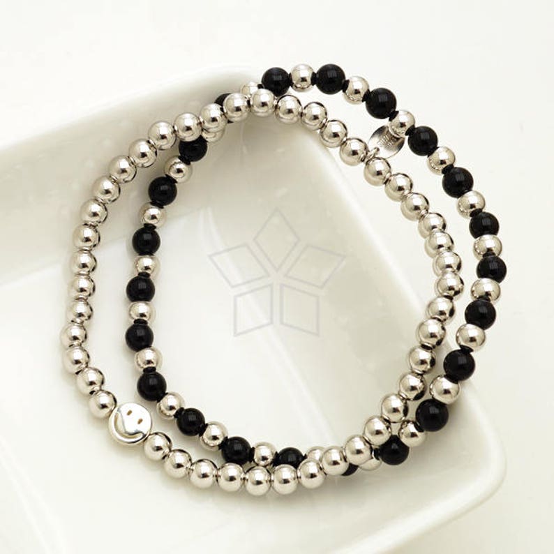 May include: A double-strand bracelet with black and silver beads. The bracelet features a silver smiley face charm.