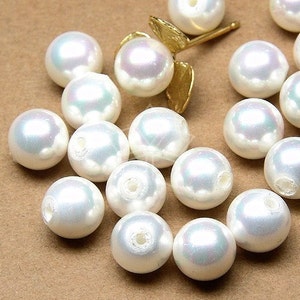 May include: A collection of white pearl beads with a slight iridescent sheen. The beads are round and have a smooth, polished surface.