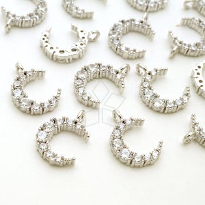 Puede incluir: Una colección de dijes de media luna plateados con acentos de cristal transparente. Cada dije tiene un bucle para sujetarlo a joyas.