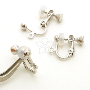 May include: Three silver clip-on earrings with clear plastic backs. The earrings have a small ball on the end of the clip.