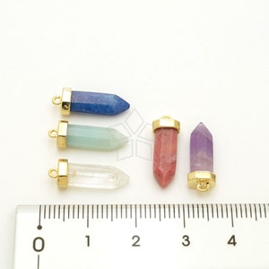 May include: Five gemstone pendants with gold-toned caps and loops. The stones are blue, green, clear, pink, and purple. The pendants are arranged on a white surface with a ruler for scale.