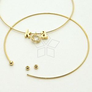 Może przedstawiać: Złoty naszyjnik z zawieszką z napisem "koa" i przezroczystym kryształem. Naszyjnik wykonany jest z dwóch cienkich, okrągłych drutów.