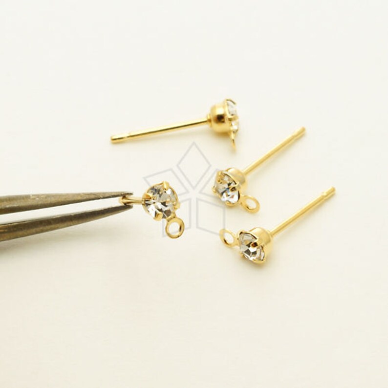 May include: Four gold earring posts with clear rhinestone accents. Two of the posts have a small loop at the end.