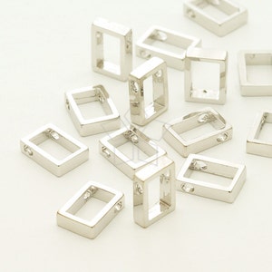 Op de afbeelding: Zilveren rechthoekige springringen van metaal met een klein gaatje aan elke kant. De ringen zijn verspreid over een wit oppervlak.