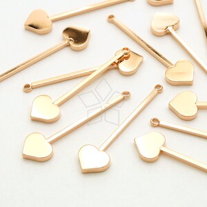 May include: A collection of gold-toned metal heart-shaped charms with a straight metal bar attached to each heart. The charms are scattered on a white surface.