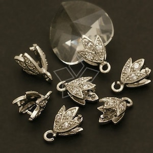 Può includere: Ciondoli pendenti in metallo argentato a forma di fiore con accenti di cristallo trasparente. I ciondoli hanno un anello nella parte superiore per essere attaccati ai gioielli.