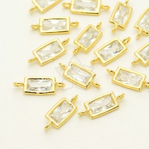 May include: A group of gold-toned rectangular crystal charms with a loop on each end. The charms are scattered on a white surface.