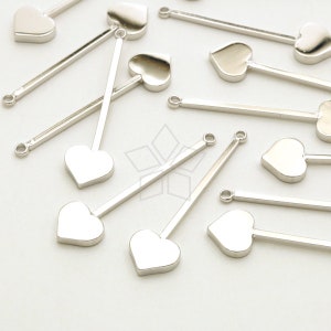 May include: Silver-toned metal charms with a heart-shaped pendant and a long, straight bar. The charms have a small loop at the top for attaching to jewelry. The heart pendants are smooth and shiny.