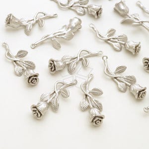 May include: A collection of silver-toned metal rose charms with detailed stems and leaves. The charms are ideal for jewellery making, scrapbooking, and other craft projects.