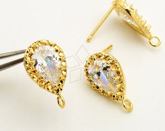 May include: Gold-toned stud earrings with a pear-shaped, clear crystal center. The crystal is surrounded by a halo of smaller crystals and a textured gold border. Each earring has a post and a small loop at the bottom.