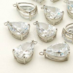 May include: A group of clear teardrop-shaped crystal pendants with silver settings. The pendants have a loop at the top for attaching to jewelry.