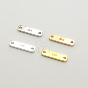 May include: Four silver and gold rectangular metal tags with rounded corners and two holes. Each tag is engraved with the number "925".