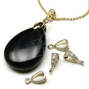 May include: A gold-colored necklace with a teardrop-shaped black pendant. The pendant is attached to a gold chain. Several gold-colored bails with clear stones are also visible, suggesting jewelry-making components. The jewelry has a shiny finish.