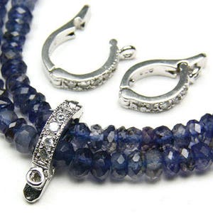 Puede incluir: Un collar de plata con una hebra de cuentas de piedras preciosas azules y un cierre de plata con cristales transparentes. El collar tiene dos cierres de plata con cristales transparentes.