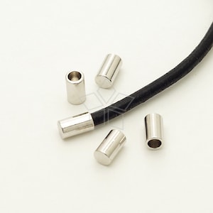 Puede incluir: Cinco tapones de cordón de metal plateado para cordón de cuero. Los tapones de cordón son cilíndricos y tienen un acabado liso y brillante.
