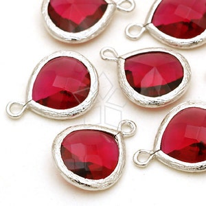 Pode incluir: Close-up de vários pingentes em forma de gota com pedras preciosas vermelhas escuras facetadas. Cada gema é definida em uma moldura prateada texturizada e tem um pequeno laço na parte superior para fixar a uma corrente ou outro componente de joia.