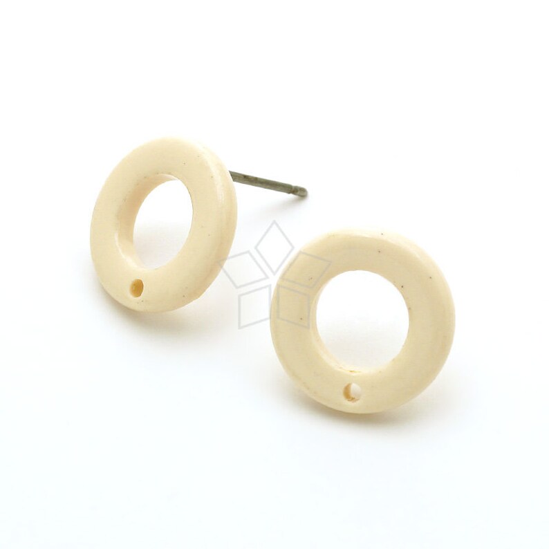 Op de afbeelding: Een paar cr&egrave;mekleurige, ronde oorbel studs met een klein gaatje in het midden van elke oorbel.