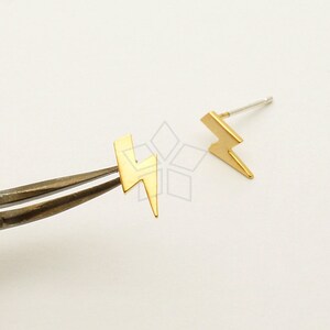 Puede incluir: Un par de pendientes de botón de rayo dorado. Los pendientes son pequeños y delicados, y serían un gran regalo para un amigo o un ser querido.