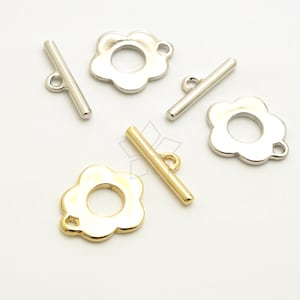 Puede incluir: Tres cierres de palanca en forma de flor, dos plateados y uno dorado, con una barra. Los cierres se utilizan para la fabricación de joyas.