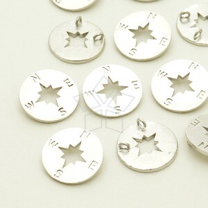 May include: Silver compass charms featuring a star design and the letters N, S, E, and W. The charms have a hole for attaching to a necklace or bracelet.