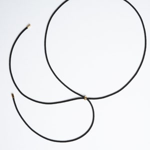 May include: A black cord necklace with a gold bead accent. The cord is tied in a knot at the back of the neck.