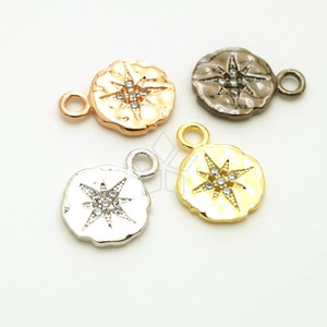 May include: Four metal compass charm pendants in rose gold, gunmetal, silver, and gold. Each pendant features a starburst design with clear crystal accents and a small loop for attaching to jewelry. The pendants have a textured, irregular edge.