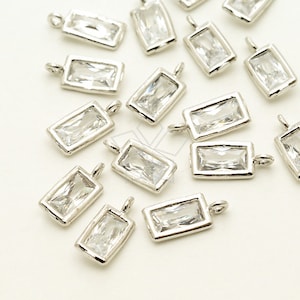 May include: A group of silver-toned rectangular charms with clear crystal accents. Each charm has a loop for attaching to a necklace, bracelet, or other jewelry.