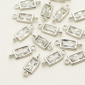 May include: A group of silver-toned rectangular connector charms with clear crystal accents. Each charm has two loops for attaching to jewelry.