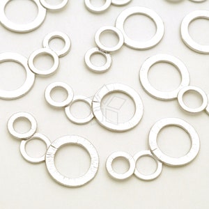 May include: Silver-coloured metal circle charms in various sizes, some connected in pairs or trios. The charms have a textured surface and are scattered across a white background, suitable for jewellery making.