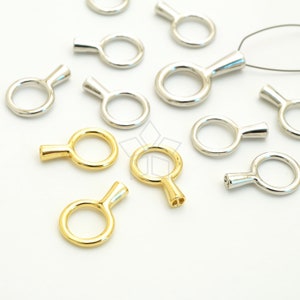 Puede incluir: Una colección de llaveros redondos de oro y plata con un pequeño asa. Los llaveros están dispuestos sobre una superficie blanca.