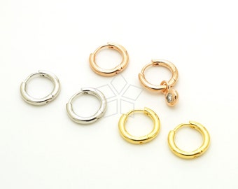 May include: A collection of small hoop earrings in silver, rose gold, and gold tones. One rose gold earring features a small, clear gemstone charm. The earrings are displayed on a white surface, showcasing their various finishes and designs.