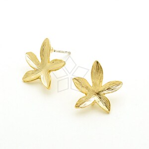 May include: A pair of gold-colored stud earrings. Each earring features a five-petal flower design with textured details. The earrings are set against a white background.
