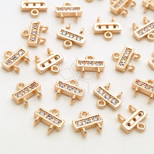 May include: Gold-toned metal connector charms with clear crystal accents. Each charm has two loops and a rectangular shape with a row of crystals.
