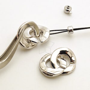 Könnte beinhalten: Zwei silberne Metallkettenglieder, jedes mit einer kreisförmigen Form und einer glatten, polierten Oberfläche. Die Glieder sind ineinander verschlungen und bilden ein dekoratives Design.