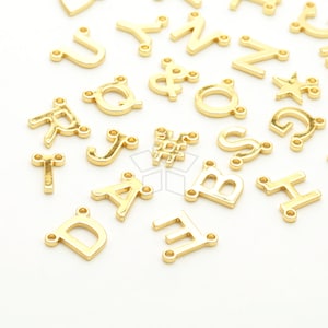 May include: A collection of gold-colored metal letter charms, including the letters A, B, D, E, F, H, J, N, Q, R, S, T, U, Y, and Z, as well as the symbols #, &, and *. The charms have two holes on each side for attaching to jewelry or other crafts.