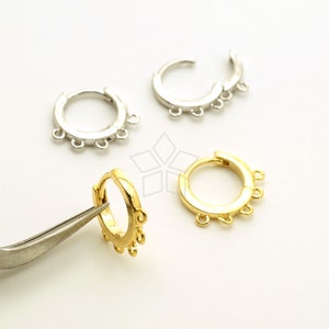 May include: Three hoop earrings with five jump rings on each hoop. One earring is gold, one is silver, and one is being held by tweezers. The earrings are on a white surface.