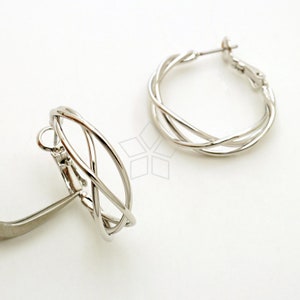 Puede incluir: Un par de pendientes de aro plateados con un diseño de alambre trenzado. Los pendientes son de estilo clip.