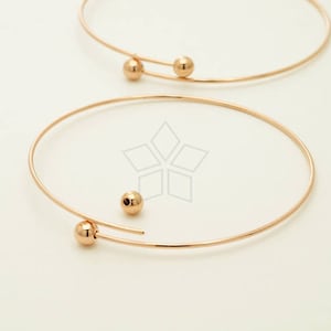 May include: Two gold hoop earrings with a small gold ball at the end of each hoop.