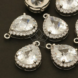 May include: A group of silver teardrop-shaped pendants with clear crystal stones and a silver halo around each stone. Each pendant has a loop at the top for attaching to a chain or cord.