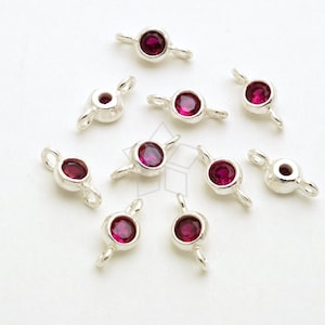 May include: Ten silver-toned jump rings with a small, round, dark pink gemstone in the center of each ring. The rings have two loops on either side of the gemstone.