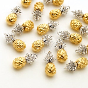 May include: A collection of gold pineapple charms with silver tops. The charms are scattered on a white surface.