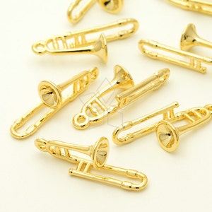 May include: A collection of small, gold-coloured trombone charms. The charms are detailed with a bell, slide, and other features of the instrument. The charms are likely for jewellery making or other craft projects.