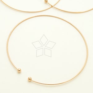 May include: A gold-toned bangle bracelet with two small round beads at the ends.