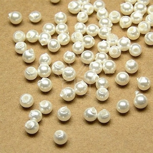 May include: A scattering of white pearl beads on a brown surface. The beads are round and have a smooth, glossy finish.