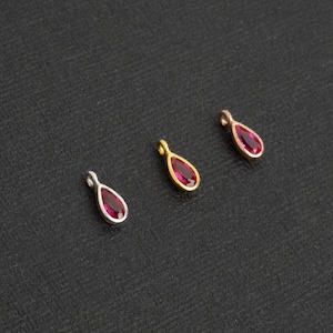 Puede incluir: Tres abalorios en forma de lágrima con una piedra preciosa roja en el centro. Los abalorios están hechos de plata, oro y oro rosa.