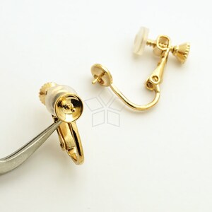 May include: Two gold-tone earring clips with a clear plastic backing. The clips are designed to hold earrings in place.