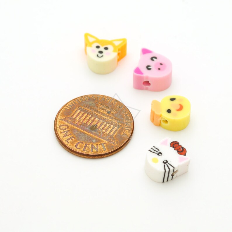 May include: Four colorful plastic animal beads with painted faces. The beads are about the size of a US penny. The beads are yellow, pink, white, and orange. The animals are a chick, a pig, a cat, and a fox.