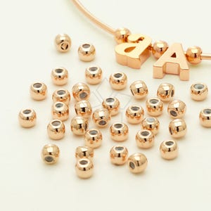 May include: A large quantity of rose gold colored metal beads. The beads are round and have a smooth, shiny finish.